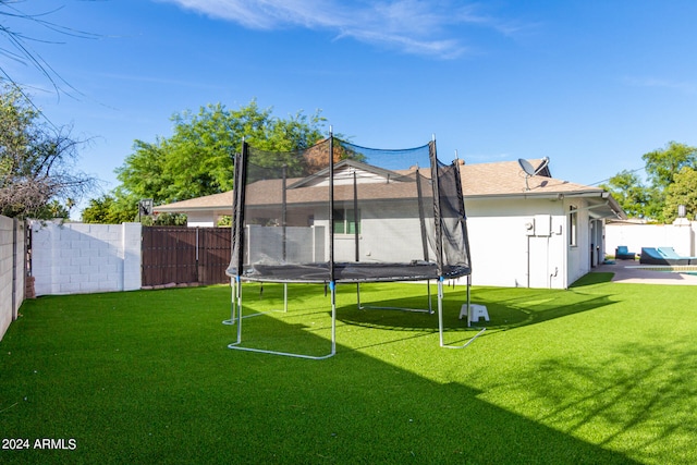 back of property featuring a trampoline, a yard, and a patio