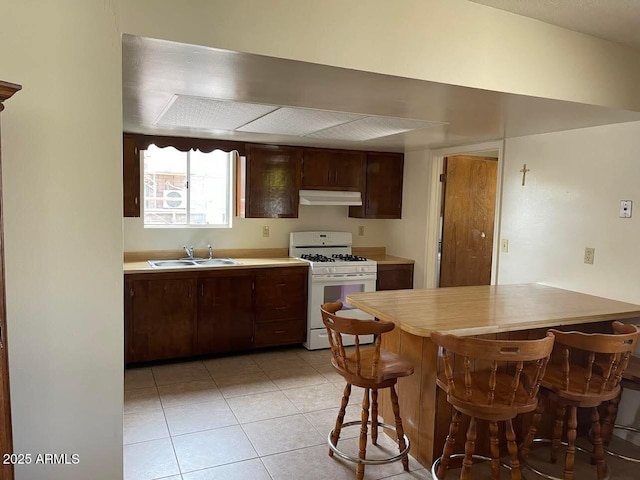 kitchen featuring under cabinet range hood, light countertops, white gas range oven, light tile patterned flooring, and a sink