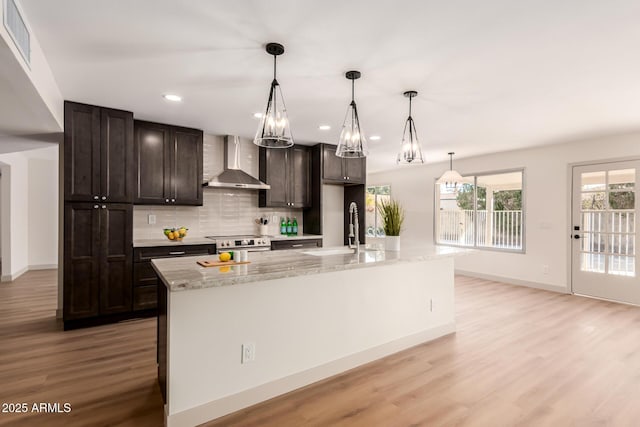 kitchen featuring a kitchen island with sink, wall chimney exhaust hood, stainless steel range with electric cooktop, and pendant lighting