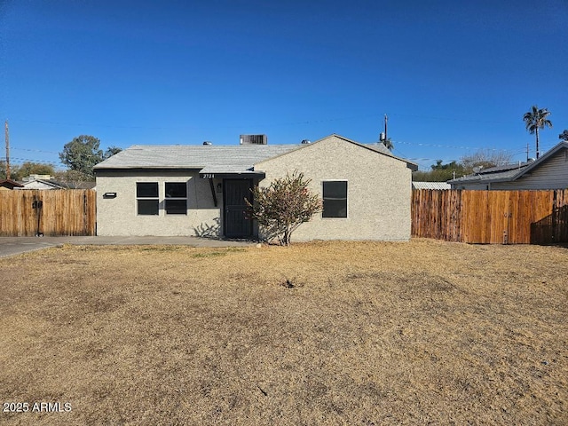 rear view of house with a yard, fence, and stucco siding