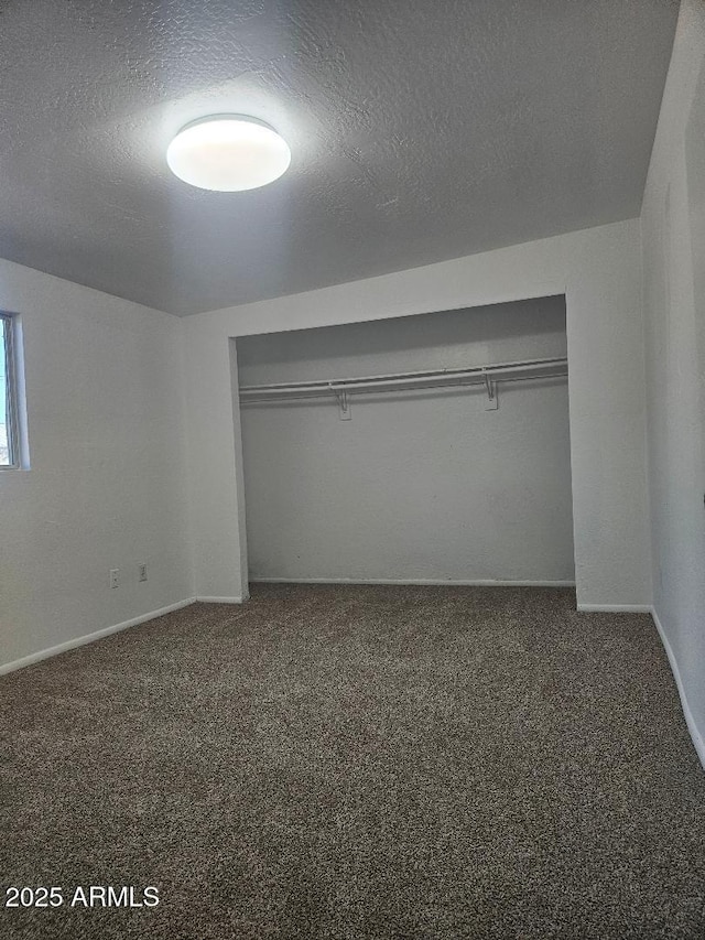 unfurnished bedroom with baseboards, a textured ceiling, dark carpet, and a closet