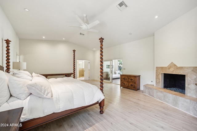 bedroom with a tiled fireplace, ceiling fan, light hardwood / wood-style flooring, and vaulted ceiling