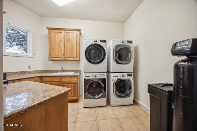 clothes washing area featuring cabinets, light tile patterned floors, sink, and stacked washer and clothes dryer