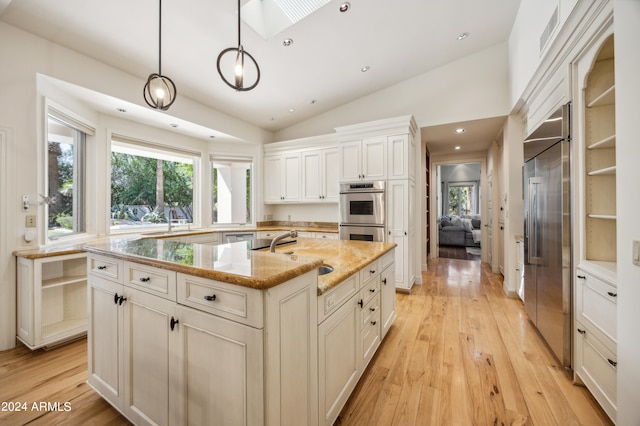 kitchen with sink, stainless steel appliances, lofted ceiling with skylight, decorative light fixtures, and a center island with sink