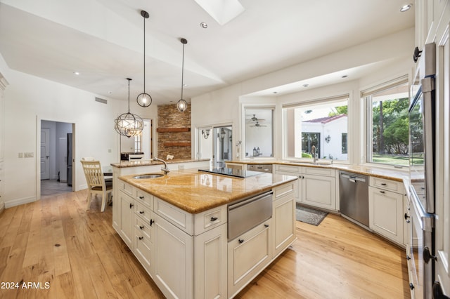 kitchen featuring a center island with sink, dishwasher, light wood-type flooring, and light stone countertops