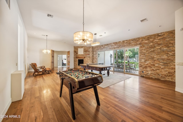 game room featuring a stone fireplace, wood-type flooring, and a chandelier