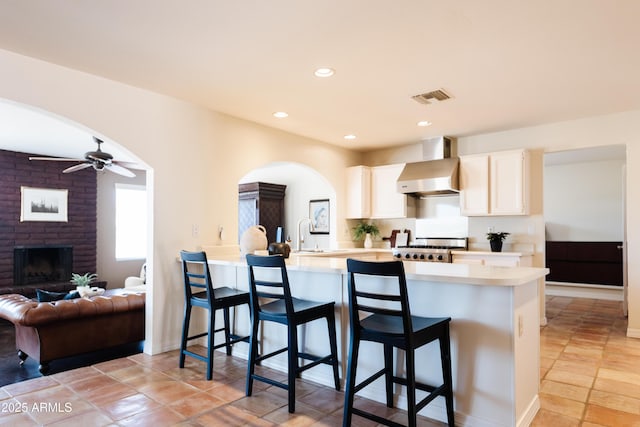 kitchen featuring a fireplace, sink, a breakfast bar area, kitchen peninsula, and wall chimney exhaust hood