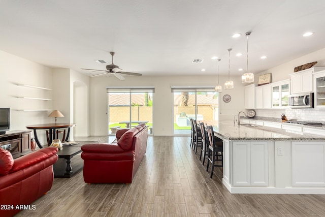 kitchen with light stone countertops, hardwood / wood-style floors, hanging light fixtures, stainless steel appliances, and white cabinets