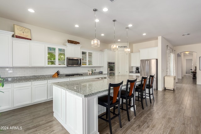 kitchen with appliances with stainless steel finishes, dark hardwood / wood-style flooring, white cabinetry, pendant lighting, and a kitchen island with sink