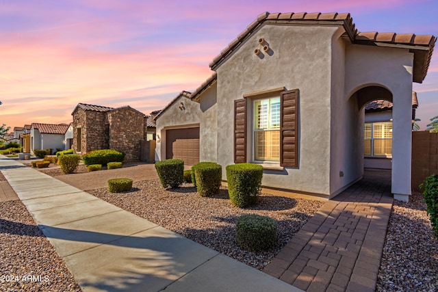 property exterior at dusk featuring a tiled roof, stucco siding, driveway, and a garage