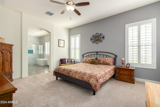 bedroom featuring multiple windows, ceiling fan, connected bathroom, and light carpet