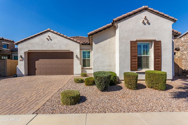 mediterranean / spanish house featuring stucco siding, decorative driveway, an attached garage, and a tile roof