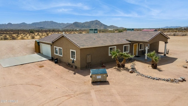 back of property featuring stucco siding, a mountain view, dirt driveway, an attached garage, and a tile roof