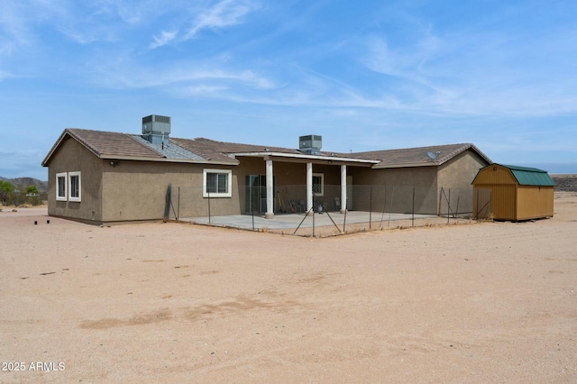back of property featuring an outbuilding, a storage shed, stucco siding, a patio area, and fence