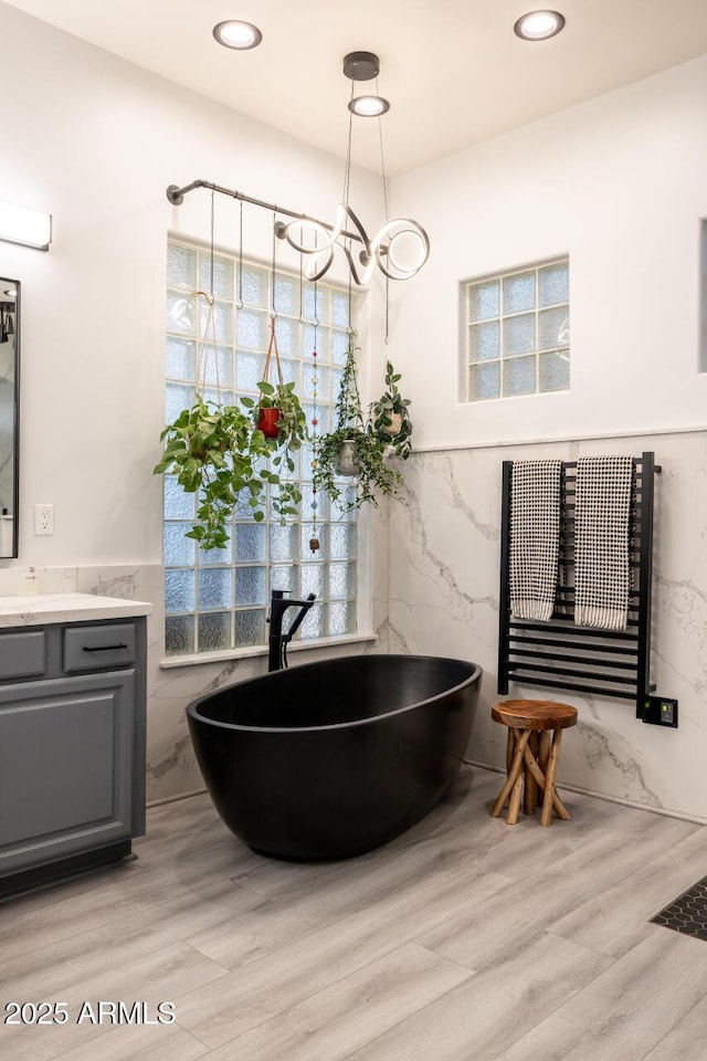8132 W Hatfield Rd, Peoria, AZ 85383 - full bath featuring tile walls, vanity, a soaking tub, wainscoting, and wood finished floors