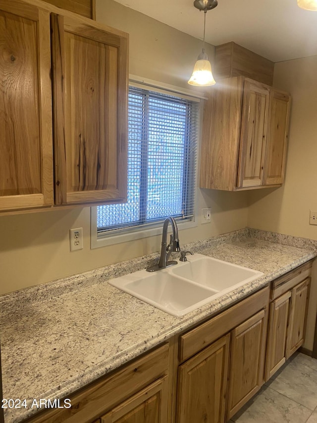 kitchen featuring light stone counters, sink, light tile patterned floors, and hanging light fixtures