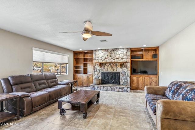 tiled living room featuring a stone fireplace, ceiling fan, and built in shelves