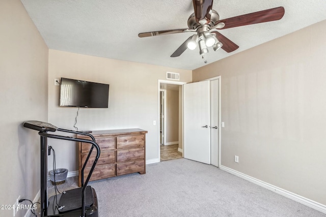 workout area with ceiling fan, light colored carpet, and a textured ceiling