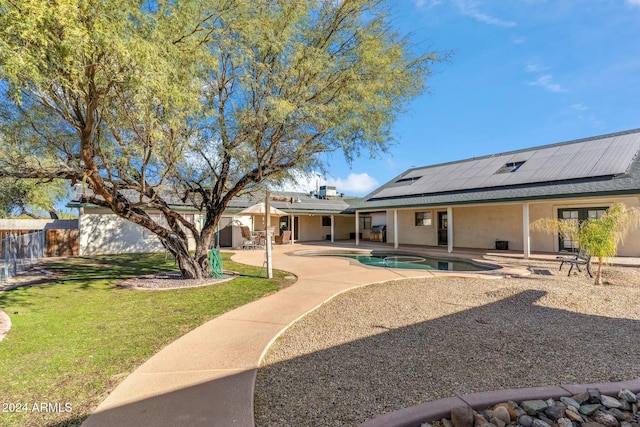 back of property with solar panels, a yard, a fenced in pool, and a patio area