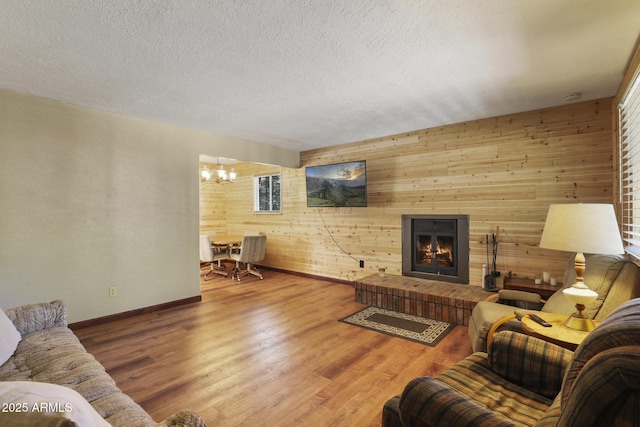 3017 Larson Loop, Forest Lakes, AZ 85931 - living room featuring a chandelier, wood walls, wood finished floors, baseboards, and a warm lit fireplace