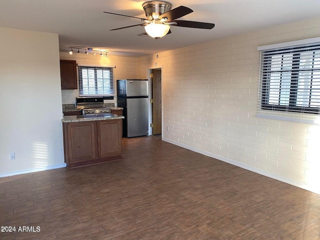 kitchen with appliances with stainless steel finishes, track lighting, brick wall, ceiling fan, and dark wood-type flooring