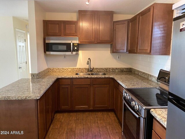 kitchen with dark wood-type flooring, sink, light stone countertops, appliances with stainless steel finishes, and kitchen peninsula