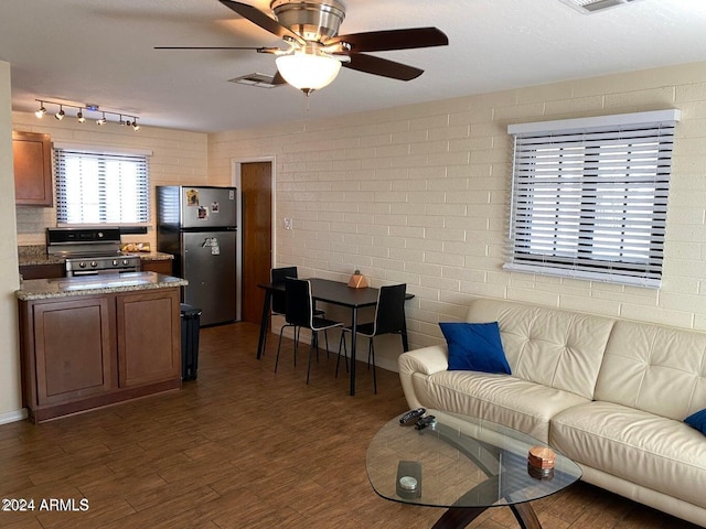 living room with ceiling fan, dark wood-type flooring, and brick wall