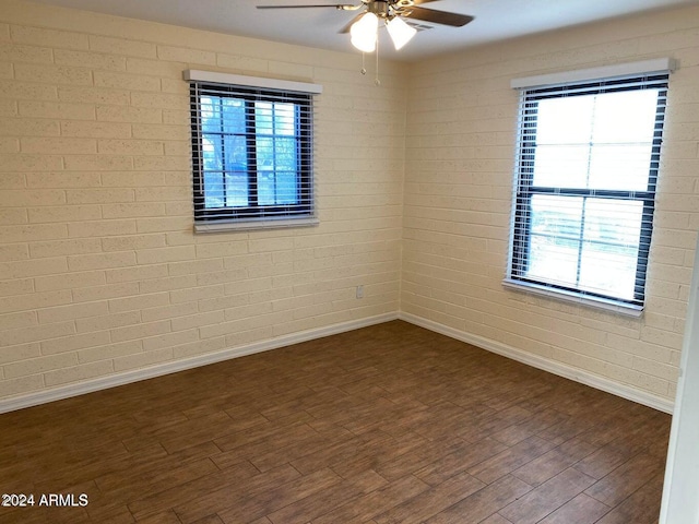 unfurnished room featuring ceiling fan, plenty of natural light, dark wood-type flooring, and brick wall