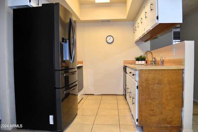 kitchen with white cabinets, light tile patterned floors, black fridge, and sink