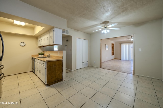 kitchen with dishwasher, sink, light tile patterned floors, a textured ceiling, and white cabinets