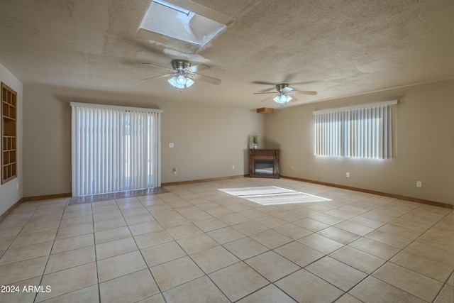 unfurnished living room featuring a skylight, ceiling fan, light tile patterned flooring, and a textured ceiling