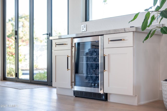 interior space featuring white cabinets, light hardwood / wood-style flooring, wine cooler, and bar