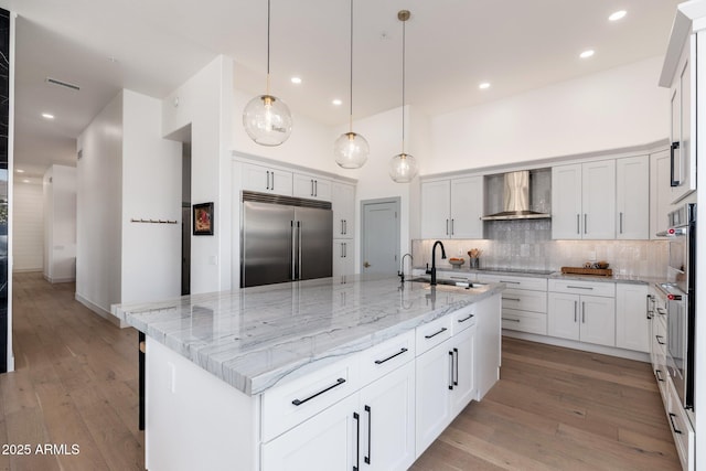 kitchen with a large island, wall chimney exhaust hood, built in fridge, backsplash, and white cabinets