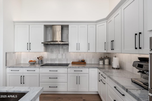 kitchen featuring light stone countertops, decorative backsplash, white cabinetry, and wall chimney range hood