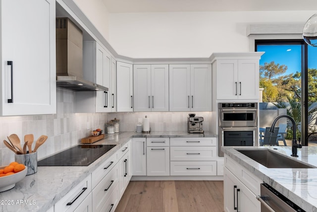 kitchen featuring appliances with stainless steel finishes, tasteful backsplash, sink, wall chimney range hood, and white cabinets