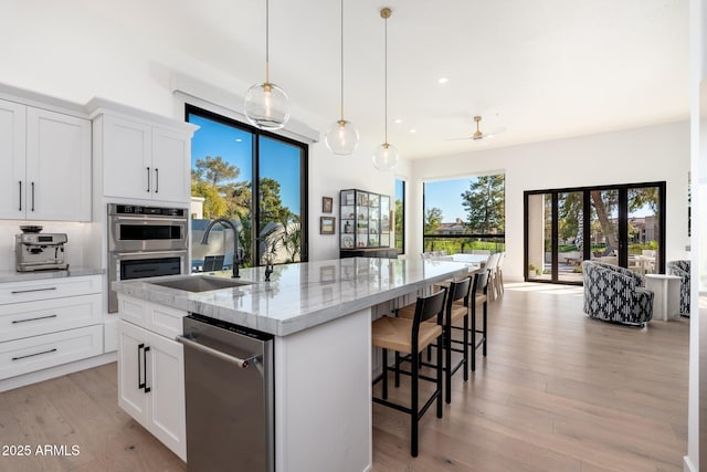 kitchen with white cabinets, a center island with sink, sink, ceiling fan, and light stone counters