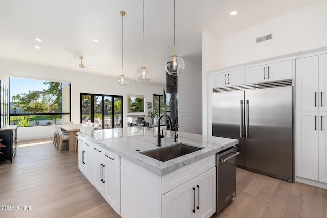 kitchen with white cabinetry, stainless steel built in refrigerator, sink, and an island with sink