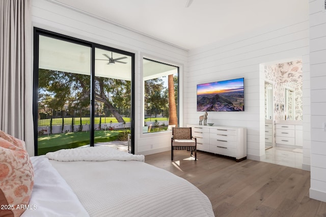 bedroom with hardwood / wood-style floors, wood walls, and access to exterior