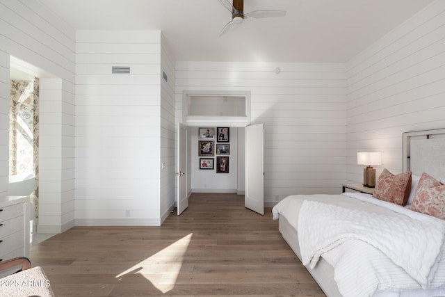 bedroom with light hardwood / wood-style flooring, ceiling fan, and wood walls