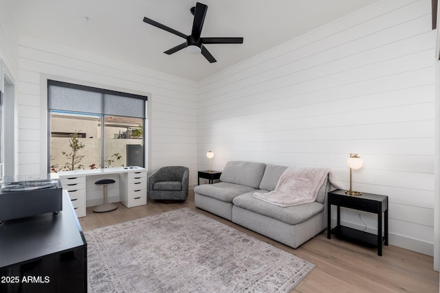 living room featuring ceiling fan, light hardwood / wood-style flooring, and wood walls