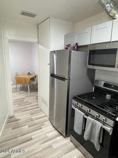 kitchen with appliances with stainless steel finishes, light hardwood / wood-style floors, and white cabinets