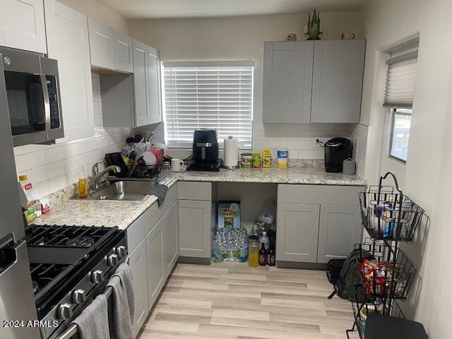 kitchen with tasteful backsplash, gray cabinets, stainless steel appliances, light hardwood / wood-style flooring, and sink