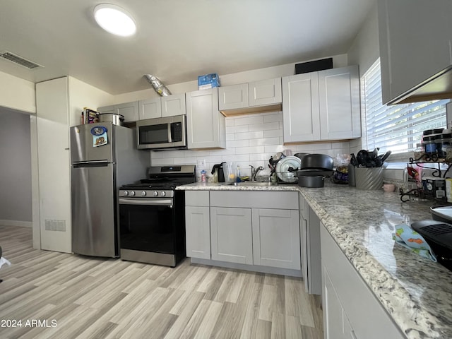 kitchen with stainless steel appliances, tasteful backsplash, visible vents, a sink, and light wood-type flooring