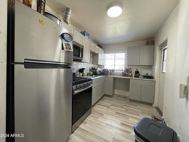 kitchen with light wood finished floors, gray cabinets, backsplash, and appliances with stainless steel finishes
