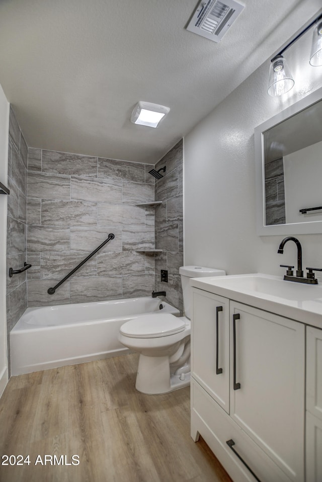 full bathroom featuring wood-type flooring, a textured ceiling, toilet, vanity, and tiled shower / bath