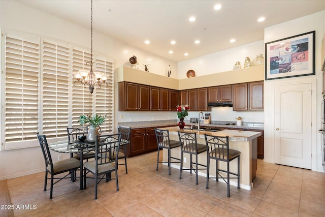 kitchen with decorative light fixtures, a center island with sink, light countertops, a chandelier, and under cabinet range hood