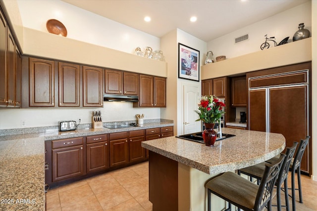 kitchen featuring a breakfast bar area, a center island, black electric cooktop, and under cabinet range hood