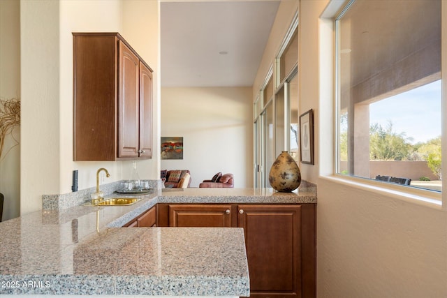 kitchen featuring a peninsula, a sink, light stone countertops, and brown cabinets