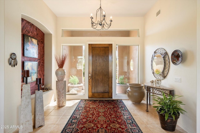 foyer featuring light tile patterned floors, visible vents, arched walkways, baseboards, and a chandelier