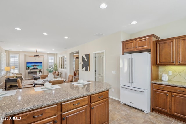 kitchen with ceiling fan, light stone countertops, high end white fridge, and backsplash